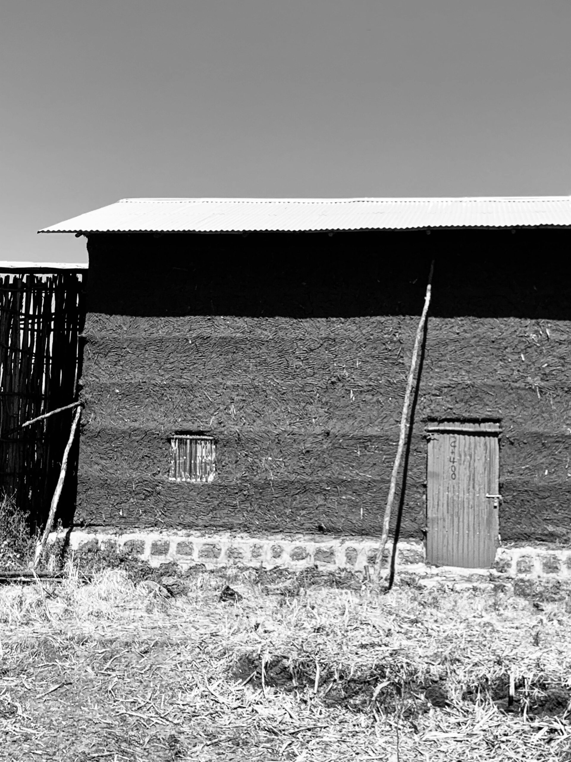Black and white photo of a rustic adobe building with wooden door and window.